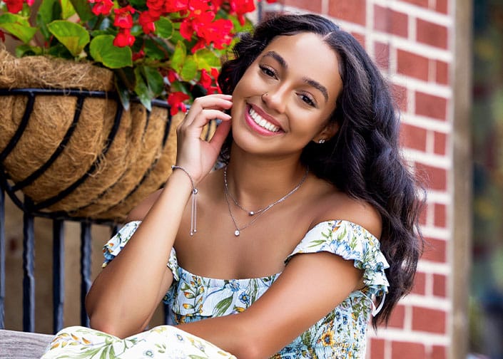 Woman wearing a floral dress sitting by flower basket on a porch.