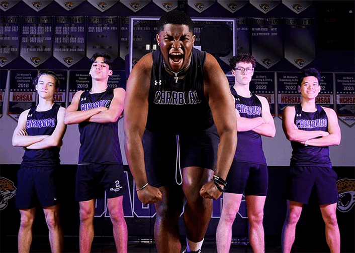 Athletic team in matching uniforms posing in a gym with championship banners in the background.
