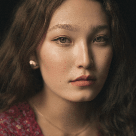 Person with curly hair wearing a red patterned garment and a pearl earring.