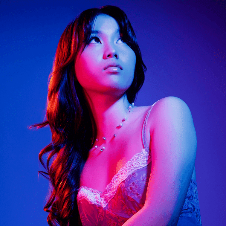 Woman in red lace dress with necklace under blue and pink lighting.