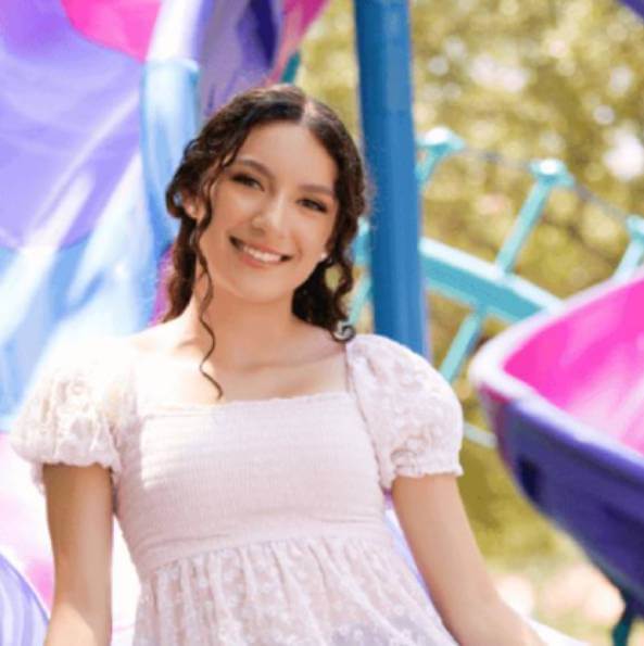 Person sitting on a purple slide at a playground, wearing a white blouse and denim shorts.