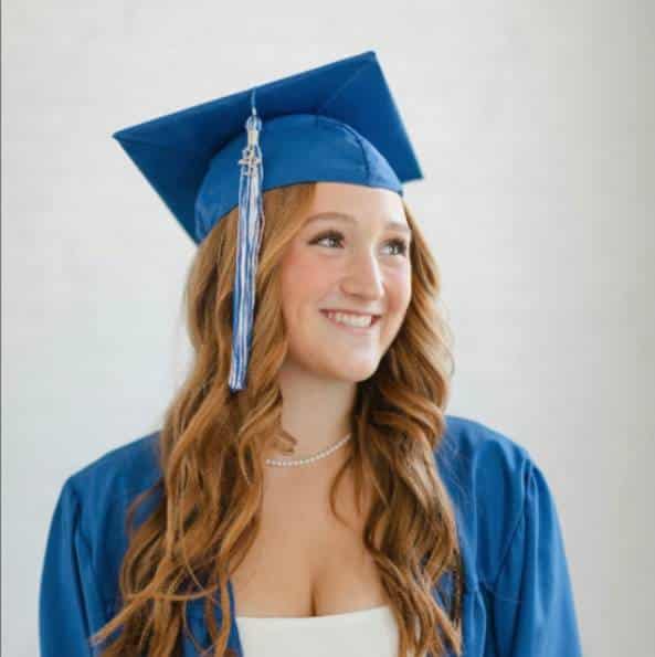 Person in blue graduation cap and gown with curly hair.